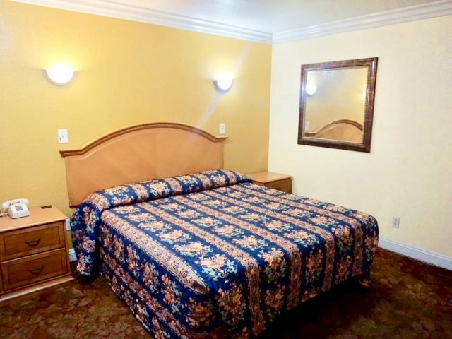 A hotel room with a bed, nightstand, mirror, and telephone.
