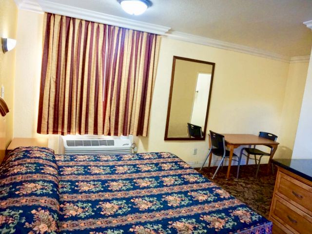 A wide view of a hotel room with a bed, dresser, table, and chairs.