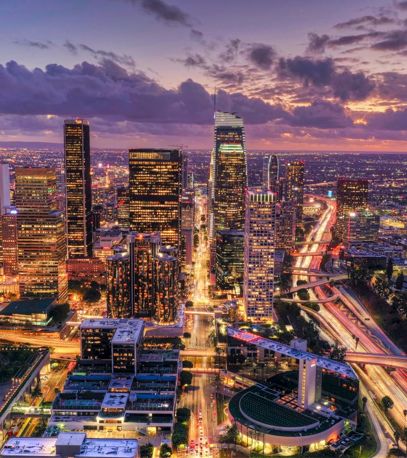Aerial view of a cityscape at sunset with skyscrapers and highway