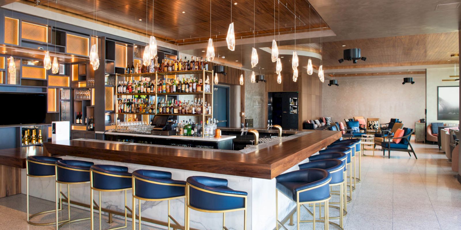 This image shows a modern bar with a large selection of bottles, elegant bar stools, and contemporary lighting fixtures.