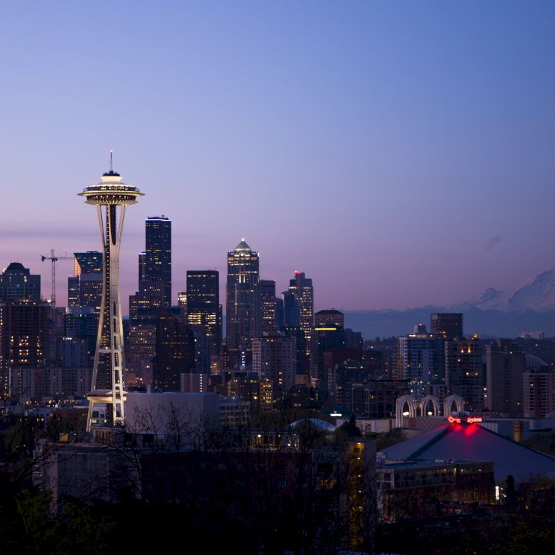 The image shows the Seattle skyline at dusk with the Space Needle prominently featured, and Mount Rainier visible in the background.