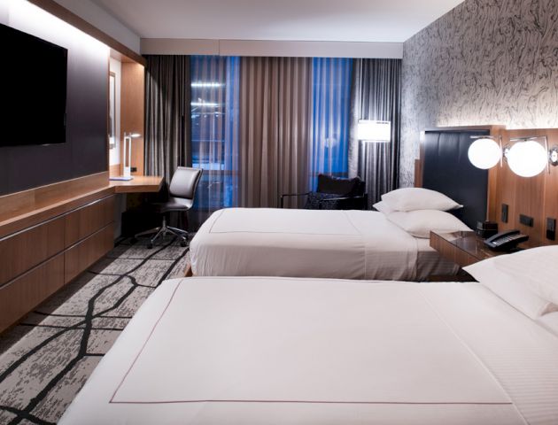 A modern hotel room with two neatly made beds, a wall-mounted TV, a desk with a chair, and stylish decor.