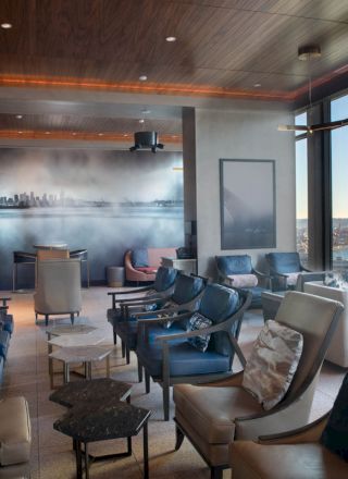 A modern lounge area with comfortable seating, large windows showcasing a scenic ocean view, and contemporary decor, including cityscape artwork.