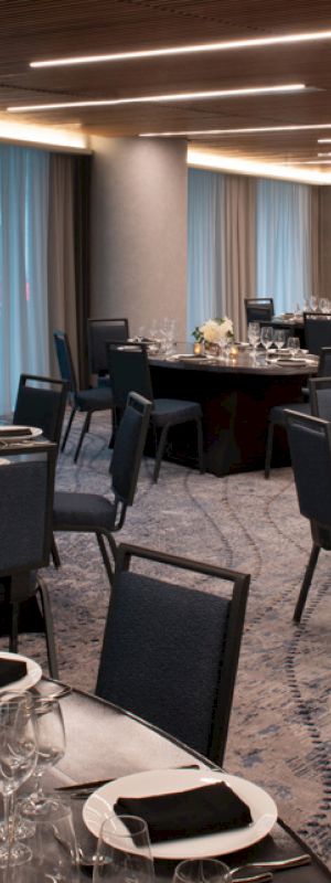 The image shows an elegant banquet hall with round tables set for a formal event, including tableware, glassware, and floral centerpieces.