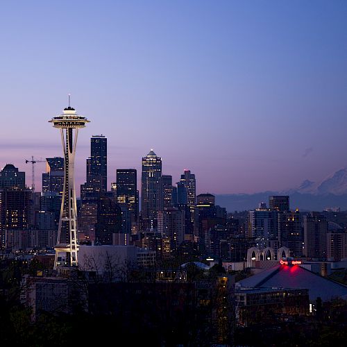 A cityscape of Seattle at dusk featuring the Space Needle with a backdrop of skyscrapers and Mount Rainier in the distance.