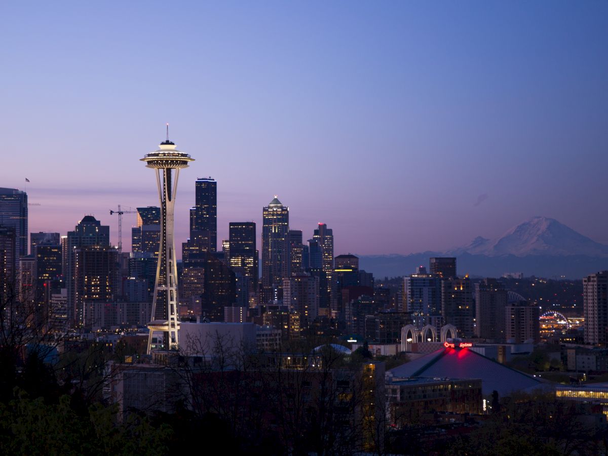 This image shows the Seattle skyline during twilight, featuring the Space Needle prominently with Mount Rainier visible in the background.