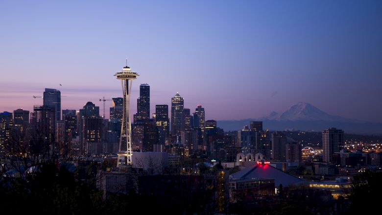 This image shows the Seattle skyline during twilight, featuring the Space Needle prominently with Mount Rainier visible in the background.