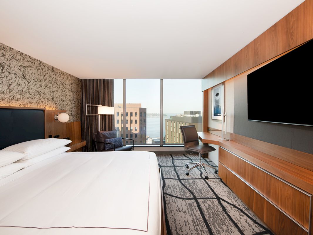 A hotel room with a large bed, TV, desk, and city view.