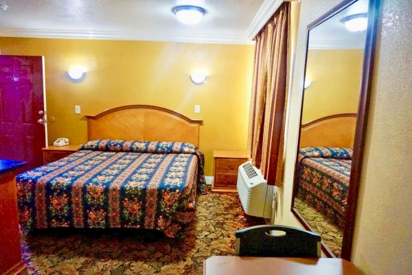 A wide view of a hotel room with a bed, nightstand, mirror, and air conditioner.