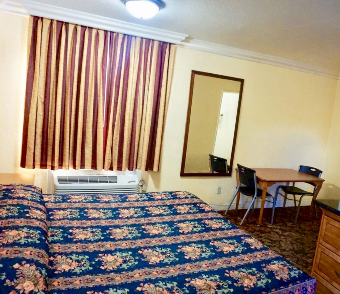 A hotel room with a bed, mirror, table, and chairs.