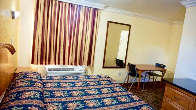 A wide view of a hotel room with a bed, desk, mirror, and air conditioner.