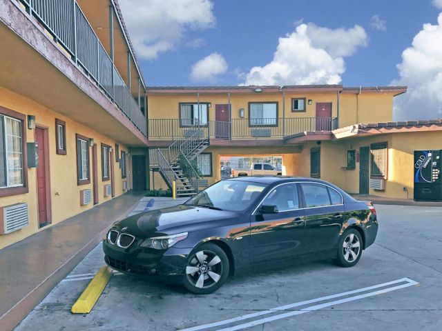 A yellow two-story motel building with a parking lot and a black car parked in front.